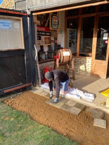 Volunteer Lee relaying floor tiles outside the Barn entrance. 